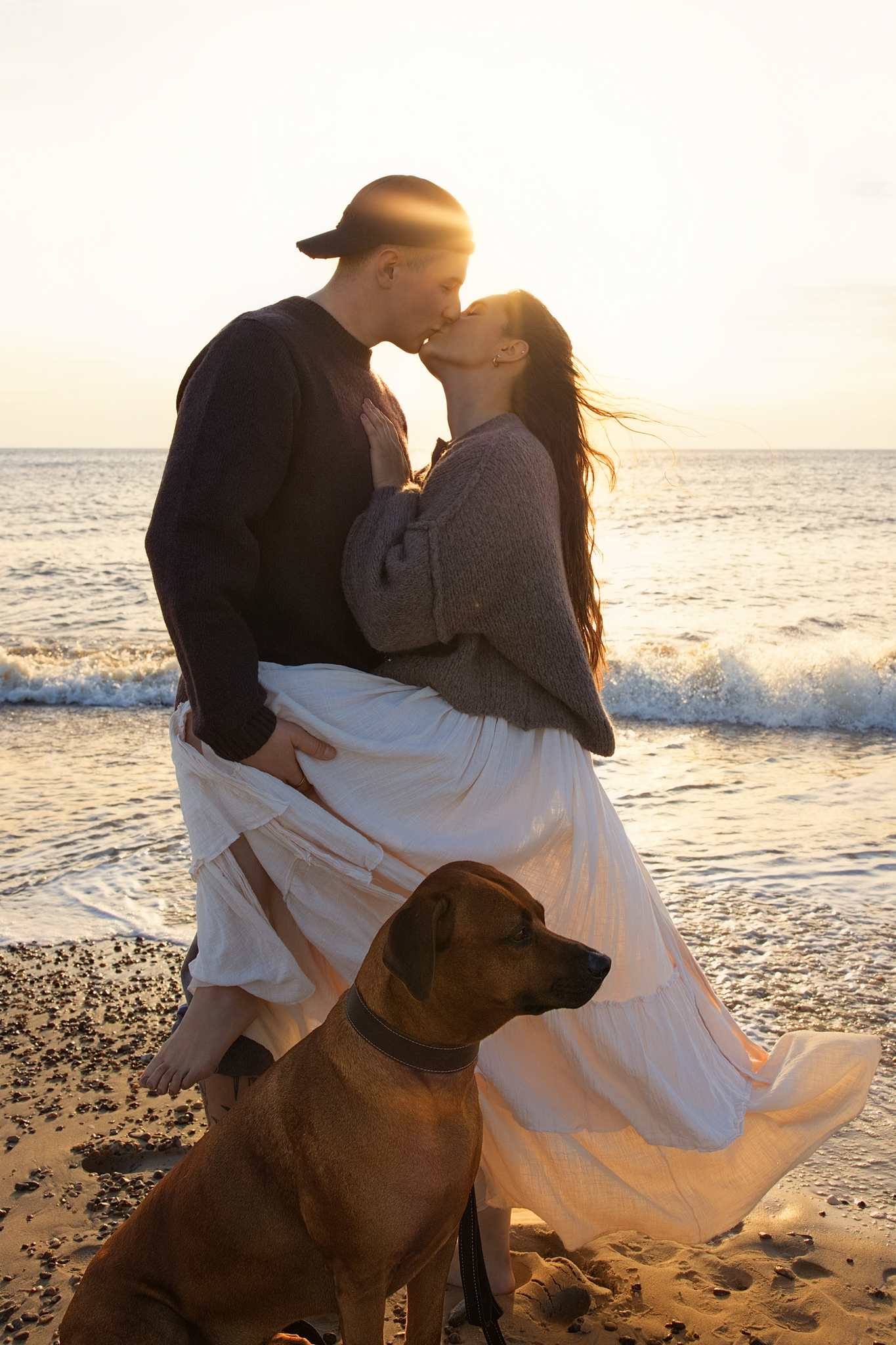 Hundefotografering i Vejers: par kysser ved stranden i solnedgang, hund sidder foran.
