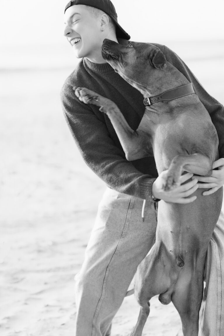 Hundefotografie in Hvide Sande: lachende Hundebesitzerin hebt großen Hund am Sandstrand