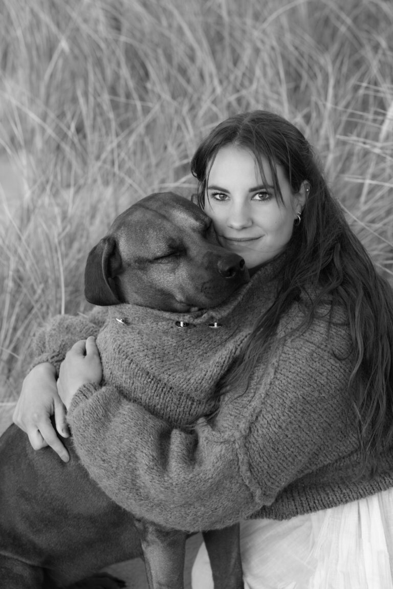 Black and white dog photography portrait in Hvide Sande: long-haired dog owner hugging a large brown dog in tall grass.